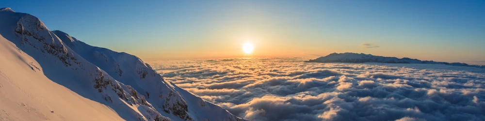 The sun sets over snow-capped mountains embedded in clouds in the Alps