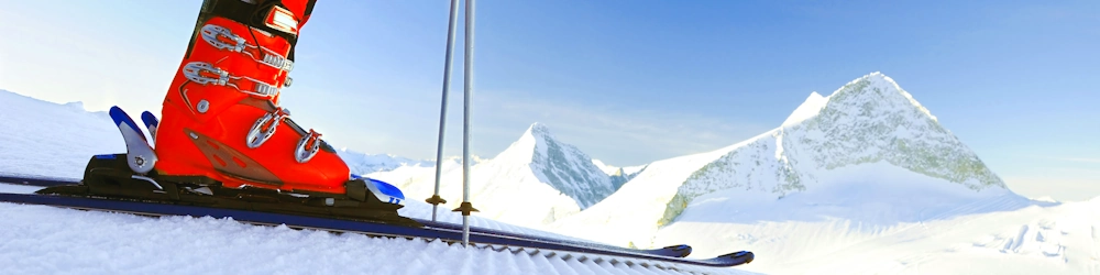 Skier with rented red ski boots standing on well-groomed slope with mountains in the background